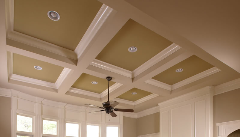 Coffered ceiling of painted white beams forming deep recessed squares, with crown molding and recessed lighting.