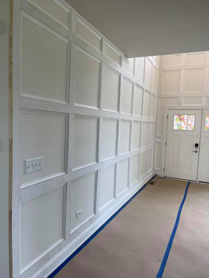 Two-story entry wall clad floor to ceiling in white square recessed panelling, mid-installation with painter's tape on the floor.